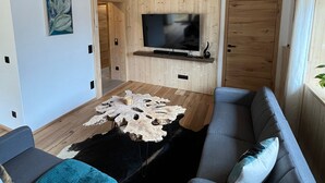 Una sala de estar moderna con techo de madera, televisor de pantalla plana en la pared, sofá gris y una mesa de centro original.
