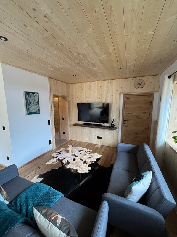 Una sala de estar moderna con techo de madera, televisor de pantalla plana en la pared, sofá gris y una mesa de centro original.