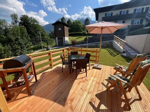 Eine Holzterrasse mit Grill, Tisch, Stühlen und Sonnenschirm.