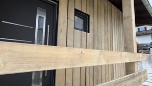 Fachada de madera con una puerta negra, un ventanal pequeño y un buzón de metal.