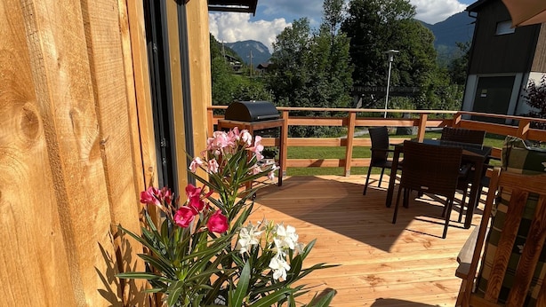 Una terraza de madera con una planta en maceta, muebles de exterior y vistas a montañas.