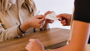Two people at a wooden table, one handing over a card with text. - Alfred Hotels Montreuil - Hôtel Rénové (Montreuil)
