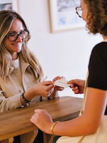 Dos personas en una mesa de madera, una entregando una tarjeta con texto.