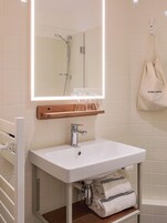 Un baño con lavamanos blanco, un espejo, toallero y ducha.