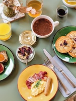 Un desayuno con tostadas, huevos revueltos, tocino, panqueques y una taza de café.