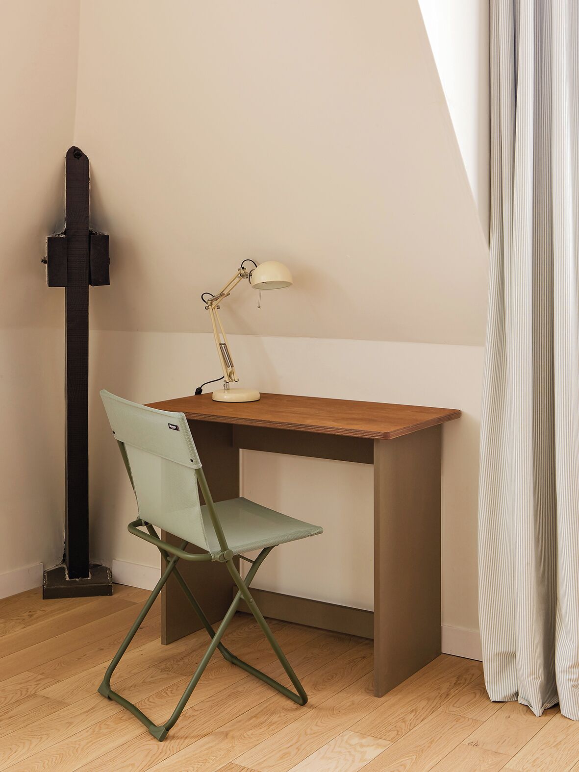 A study area with a desk, chair, lamp, and a black vertical object.