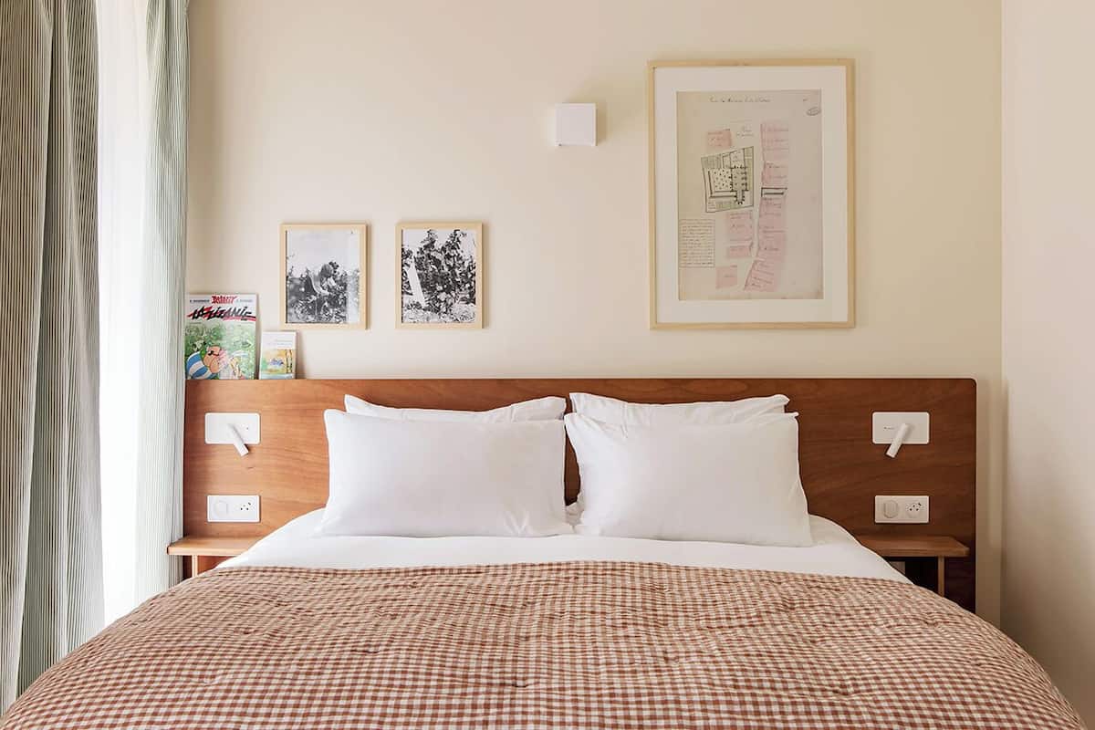 A hotel room with a large bed, two framed pictures on the wall, and a window with curtains.