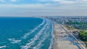 Luchtbeeld van een kuststad met een breed strand, een dichtbebouwd stedelijk gebied en een heldere lucht.