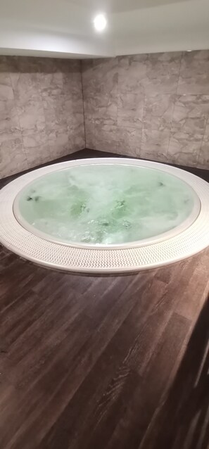 A hot tub in a room with a marble wall and dark wooden floor.