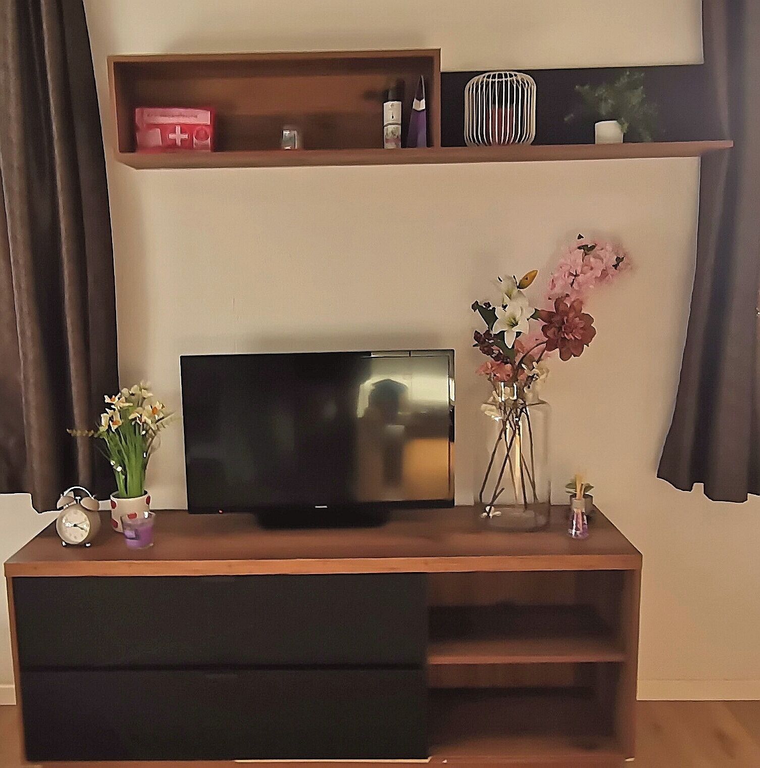 A flat-screen TV on a wooden TV stand with a shelf above it.