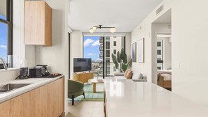 Una cocina moderna con armarios de madera, un comedor con sofá verde, un televisor de pantalla plana y un amplio ventanal con vistas a la ciudad.