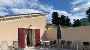 Une terrasse avec une table et des chaises, une porte rouge et une vue sur les arbres et les montagnes.