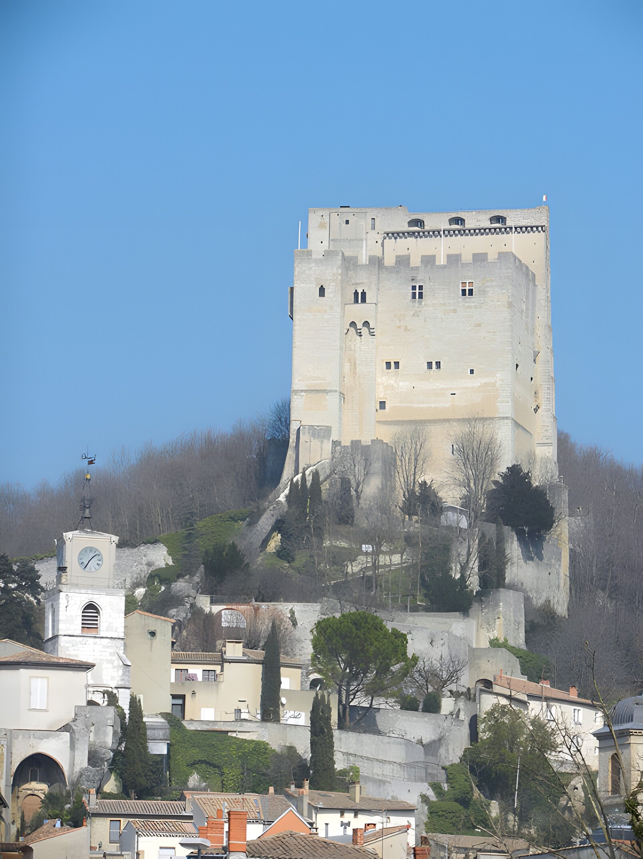 A historic castle-like structure with a clock tower, situated on a hill with surrounding buildings.