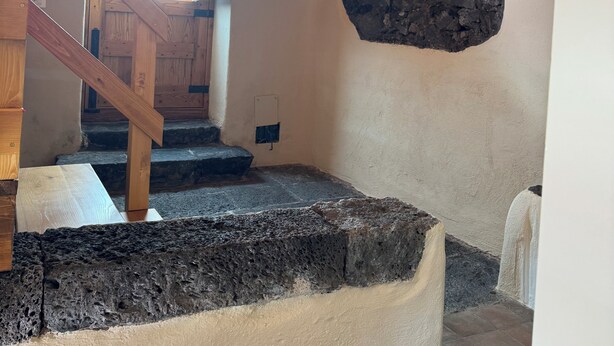 Eine Treppe mit hölzernen Geländern und Steinstufen, die zu einer Tür mit Holzrahmen führt.