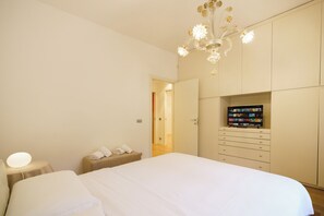 Ein Schlafzimmer mit einem großen Bett, einem Nachttisch mit Lampe, einem Kleiderschrank mit integriertem Fernseher und einer Deckenleuchte.