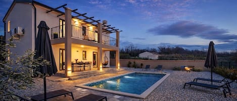 Uma casa de dois andares com piscina, área de estar externa e pérgola.
