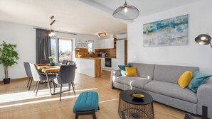 A modern living room with a grey sofa, blue and yellow cushions, a round coffee table, and a dining area with a wooden table and grey chairs. - Villa Lumina Divina-Modern villa with Heated Pool (Prhati)