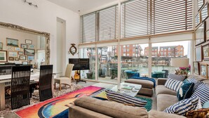Un salon spacieux doté d’une grande fenêtre, un coin repas avec une table et des chaises, et un coin salon confortable avec un canapé et des coussins.