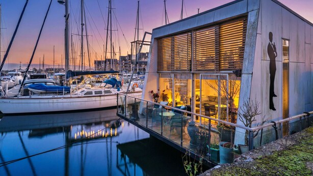 Un bâtiment moderne à la façade vitrée, donnant sur une marina où sont amarrés des bateaux.