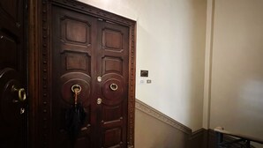 Una porta doble de fusta amb un mànec de bronze i un ull de cerradura, un interruptor de llum petit, i una escala de marbre amb un estraperç rayat.