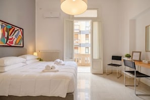 A hotel room with a bed, a desk, a chair, a radiator, and a window with a view of buildings. - Spacious & Serene Apartment (Bari)