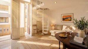 Un saló modern amb una escala espirall, un sofà, una taula de centre amb aperitius i un quadre a la paret.