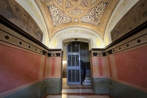 A grand hallway with ornate ceiling decorations, a staircase, and a door with a number plate. - Spacious & Serene Apartment (Bari)