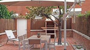 A patio with a wooden table and chairs, a brick barbecue, and a white door. - House in Palafolls Near Costa Brava Beaches (Palafolls)
