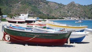 Una playa con barcos amarrados, montañas al fondo y cielo despejado.