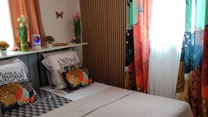 A bedroom with a bed, a shelf with decorative items, an air conditioner, and curtains.