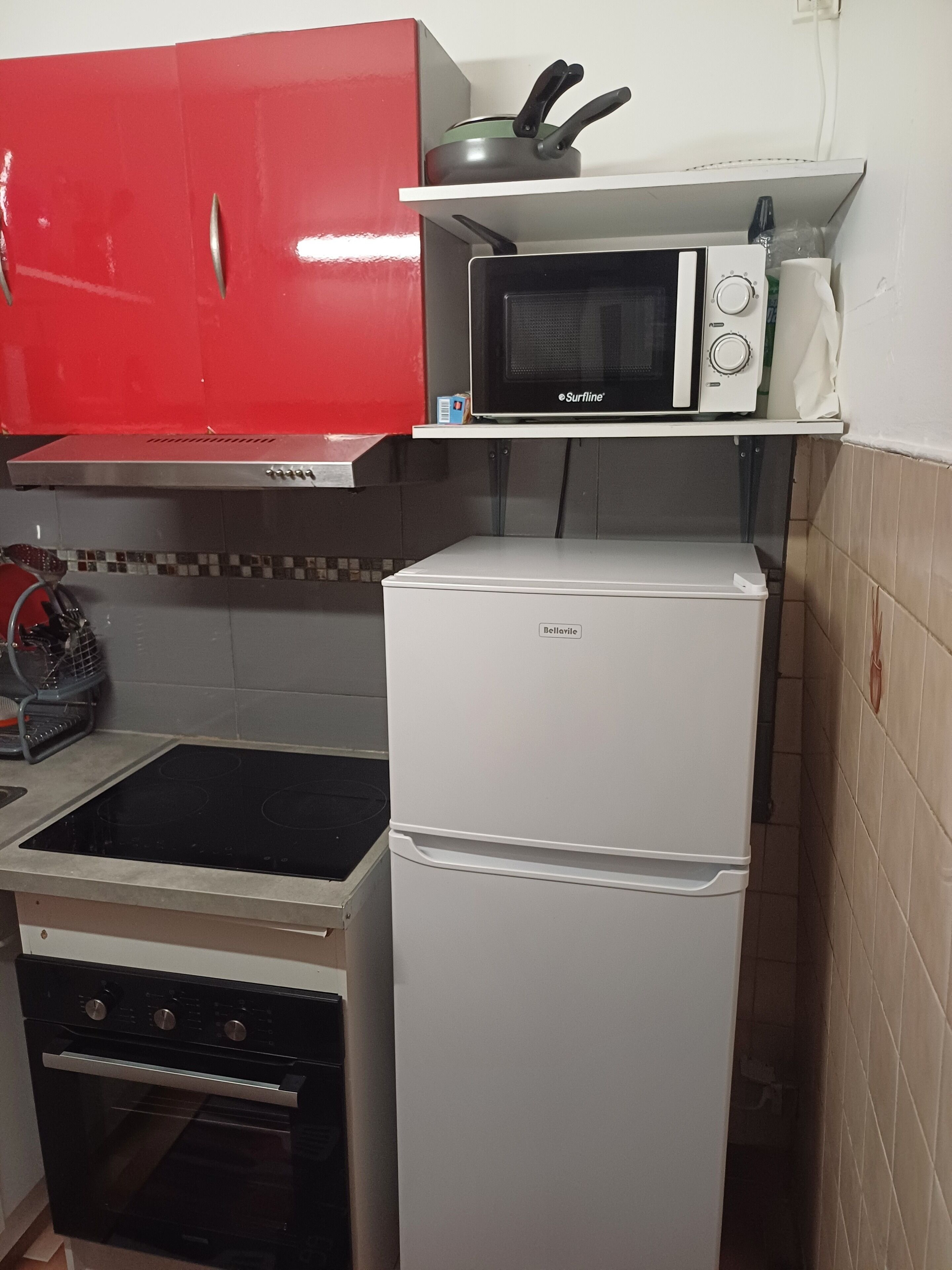 Une cuisine de taille réduite avec un meuble rouge, un micro-ondes blanc et un réfrigérateur blanc.
