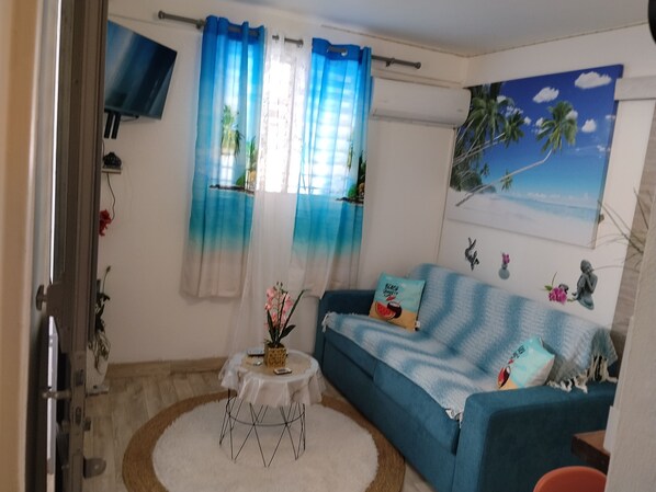 Una sala de estar con un sofá azul, una mesita redonda y un tapete blanco.