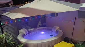 A hot tub with a white umbrella, surrounded by greenery and string lights.
