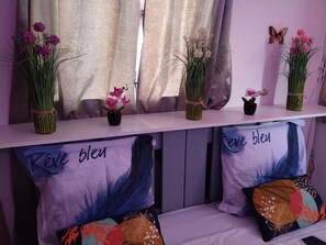 Ein Zimmer mit einem weißen Regal, das verschiedene Blumenarrangements zeigt, und zwei Kissen mit der Aufschrift 'Rêve bleu'.