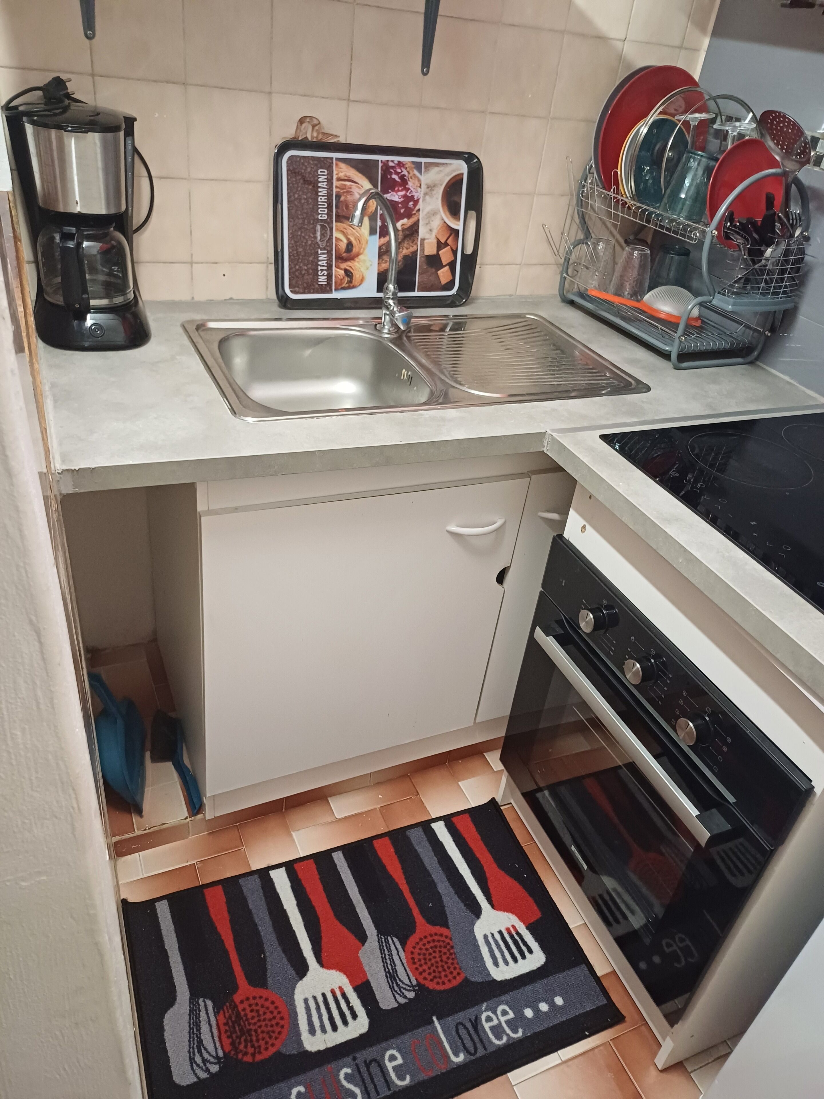 Una cocina compacta con un lavamanos, una cafetera, un escurreplatos y una estufa.