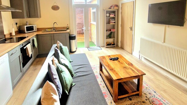 A compact living space with a kitchenette, a sofa with cushions, a wooden coffee table, and a television mounted on the wall. - City Stay Worcester - free parking (Worcester)
