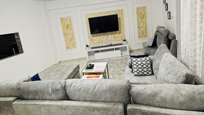Een moderne woonkamer met een grijze hoekbank, een flatscreen televisie aan de muur en een witte entertainmentkast.