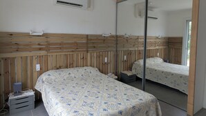 A bedroom with a bed, a mirror, an air conditioning unit, and a wooden headboard.
