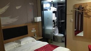 Habitación de hotel con cama, zona de ducha y espejo.