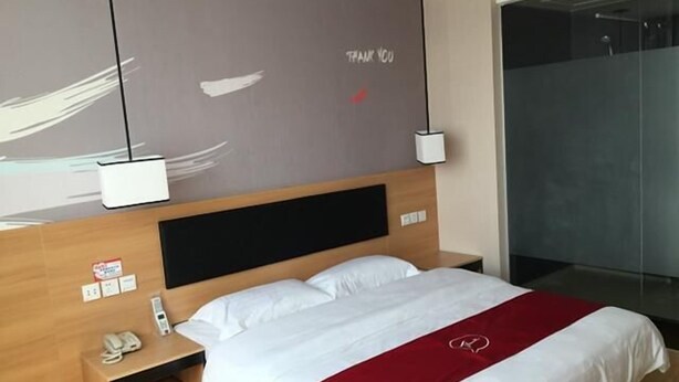 Habitación de hotel con cama, mesita de noche con teléfono, un detalle rojo en la colcha y un cartel en la pared que dice 'THANK YOU'.
