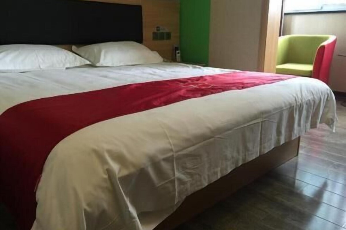 A bed with a white and red bedspread, a wooden headboard, and a green wall in the background.