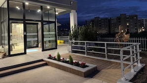 A modern building with large glass windows, a wooden deck with planters, and a white railing. - Floris Hotel (Rende)