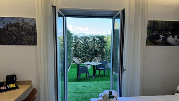 A hotel room with a bed, a desk with a coffee maker, and a view of a garden with a table and chairs. - Floris Hotel (Rende)