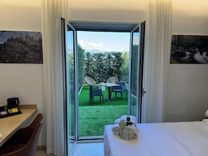 Une chambre d’hôtel avec un lit, un bureau doté d’une machine à café et une vue sur un jardin aménagé avec une table et des chaises.