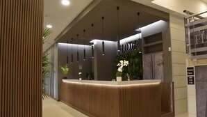 A modern reception desk with a wooden finish, pendant lighting, and a sign indicating the floor level. - Floris Hotel (Rende)