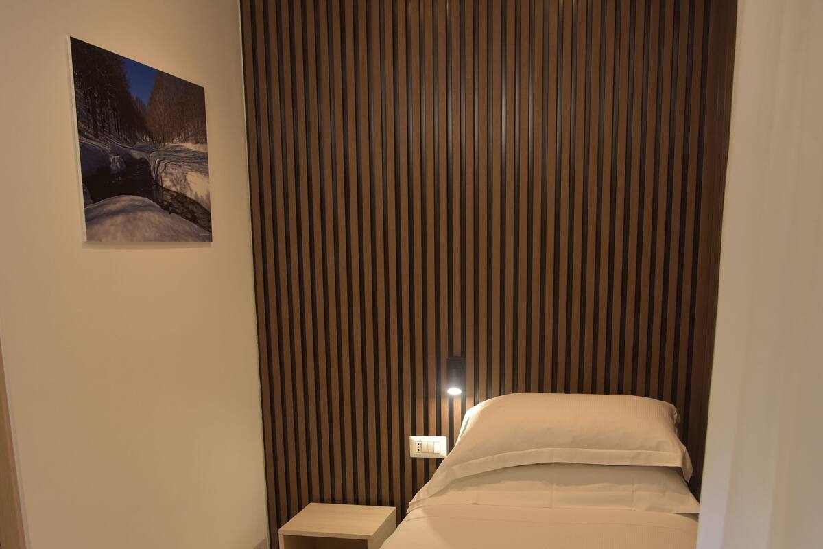 A neatly made bed with white linens, a small bedside table, and a wall-mounted light.