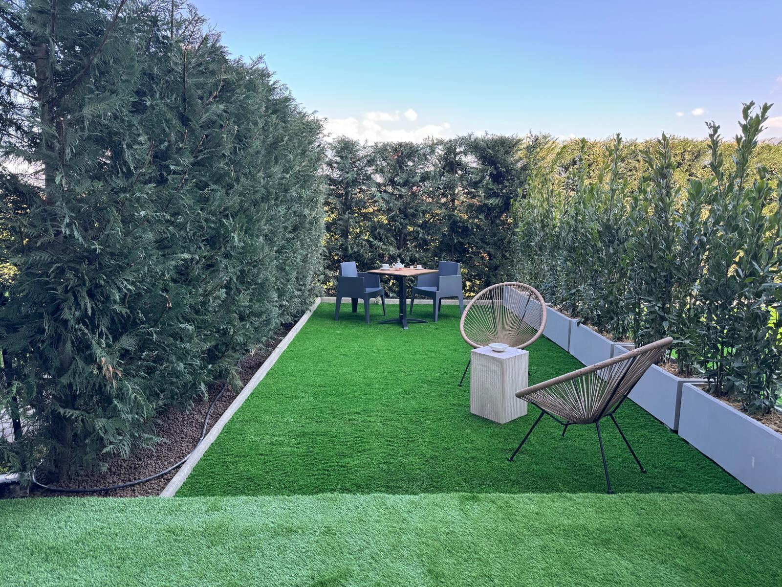 Une terrasse avec un revêtement de gazon synthétique, une table, des chaises et un fauteuil décoratif.