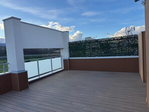 Eine moderne Außenterrasse mit Holzboden, weißen Wänden und Blick auf einen Fluss und Berge.