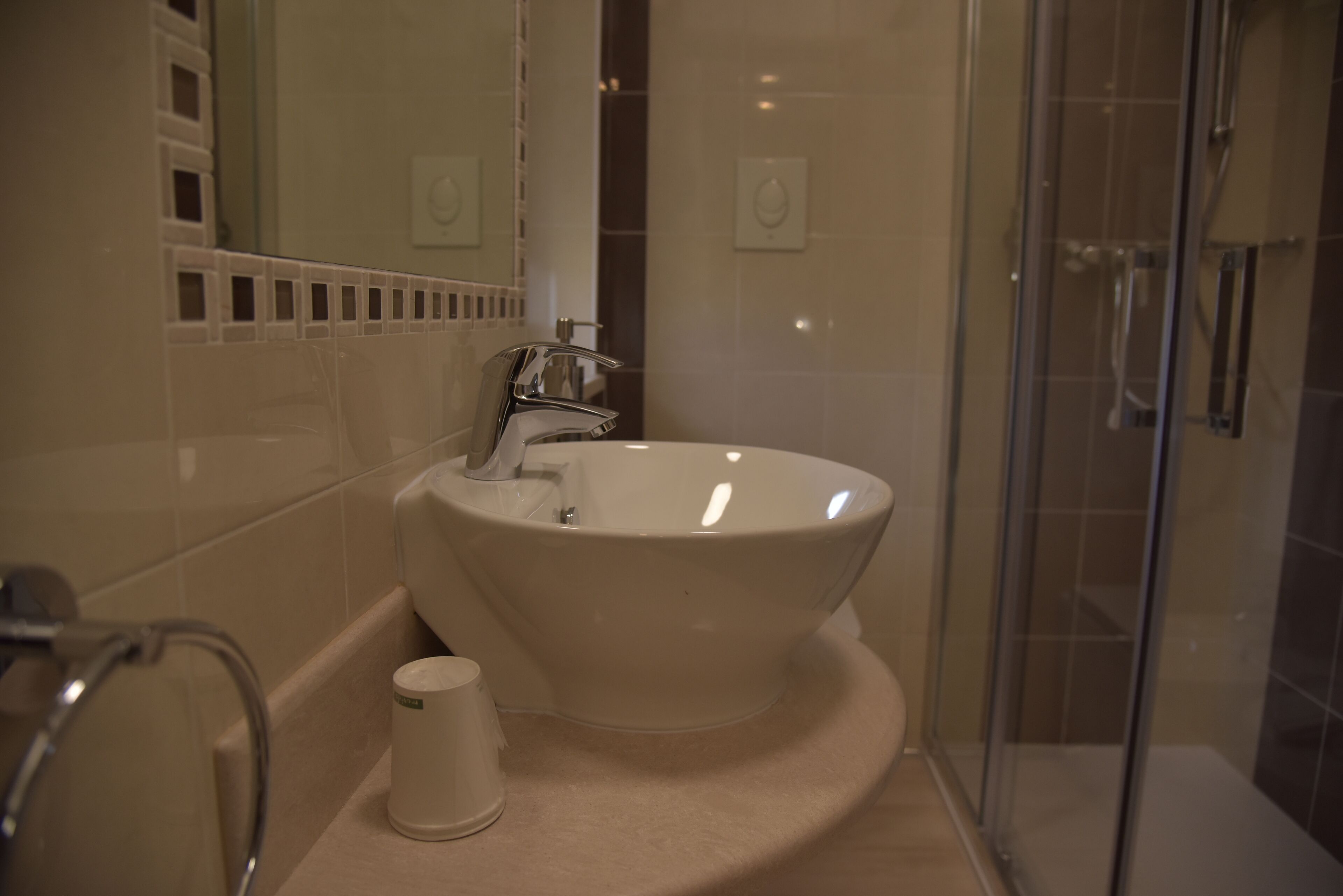 Un baño con un lavabo grande de color blanco, cabina de ducha con paredes de vidrio y un inodoro con dispensador de toallas de papel.