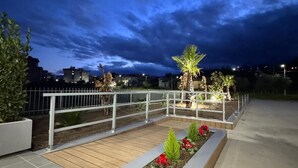 A rooftop garden with a wooden deck, metal railing, and potted plants. - Floris Hotel (Rende)